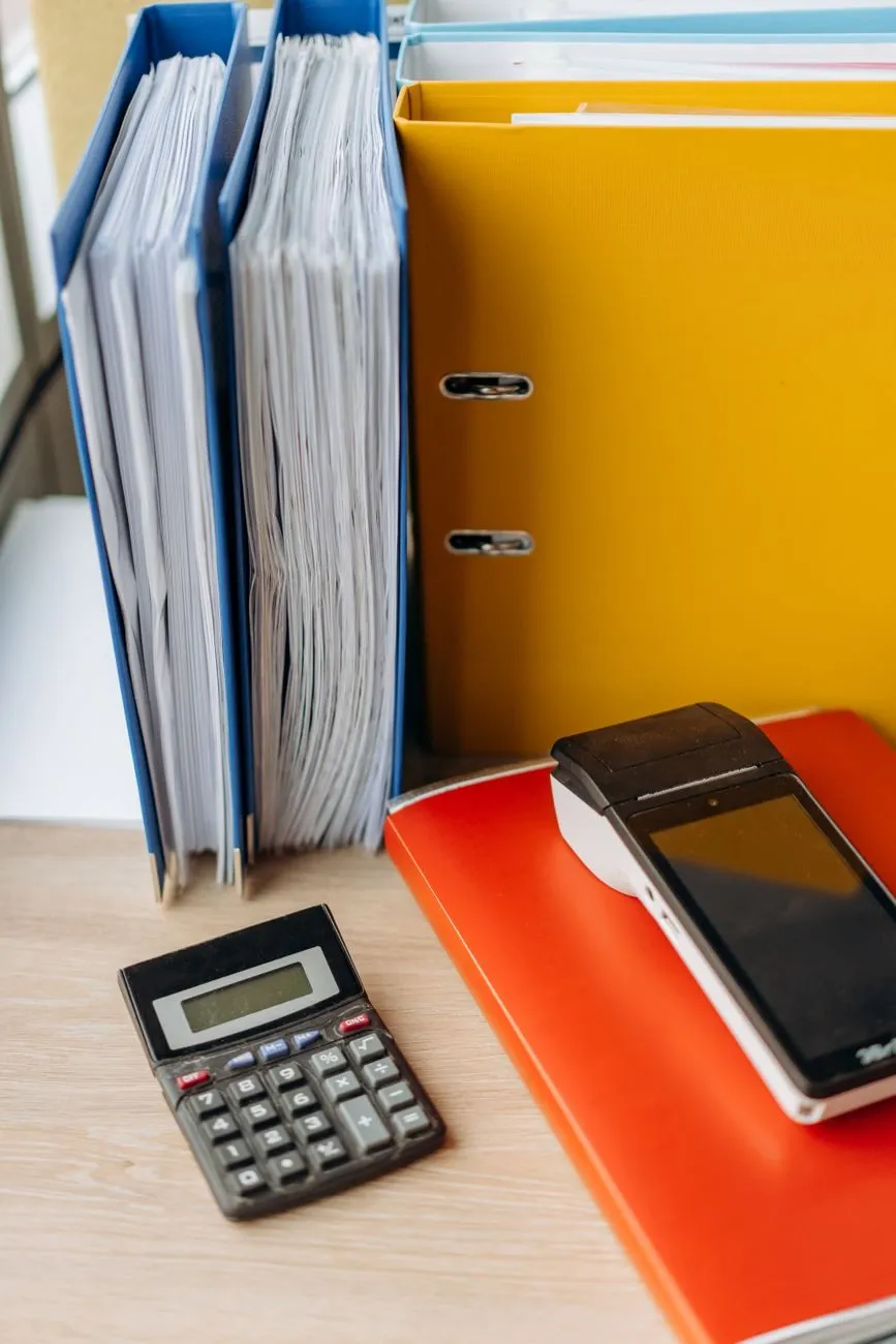 Blue and yellow lever-arch files standing on a desk beside a calculator
