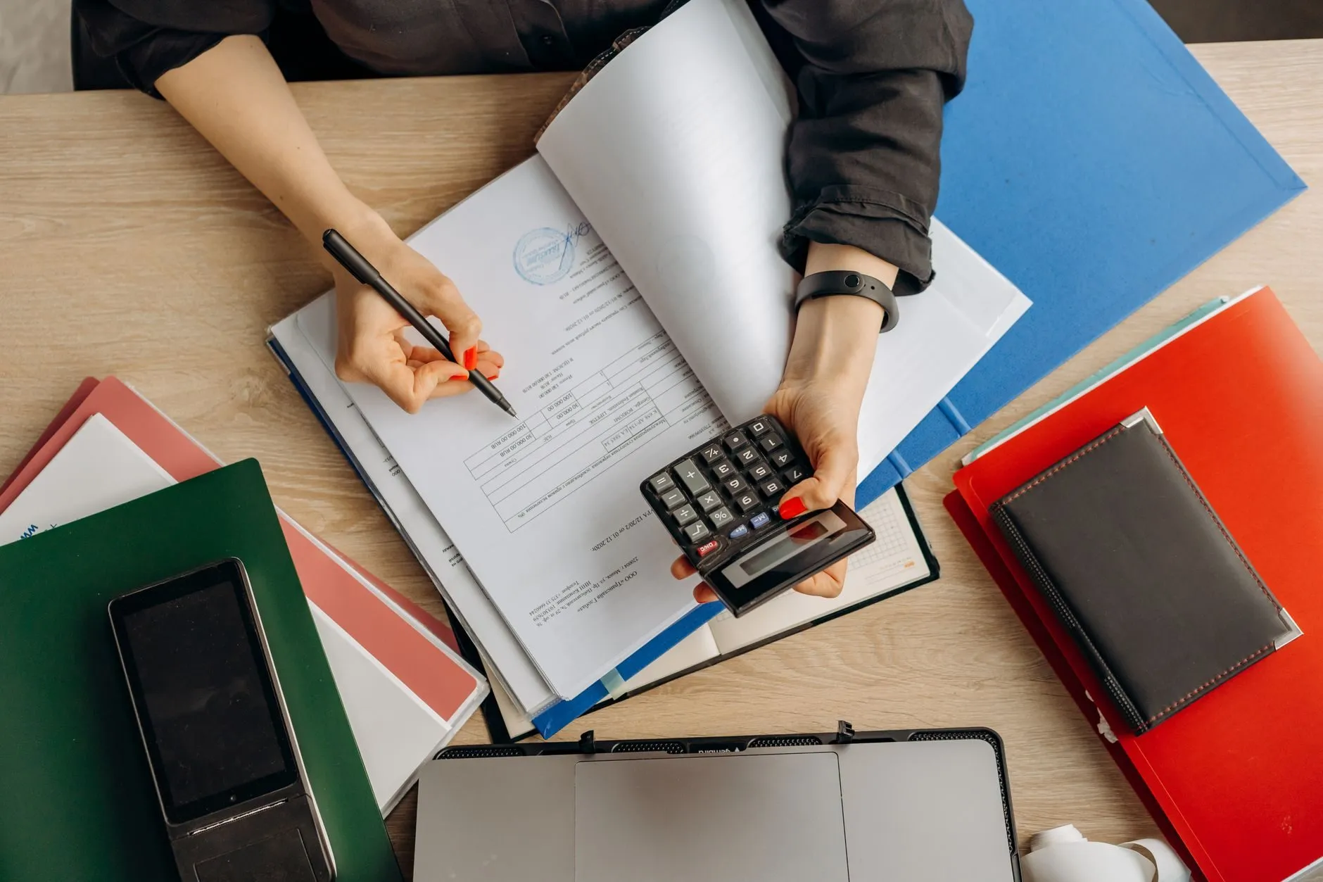 Overhead view of an accountant checking a stamped invoice against a calculator, with coloured folders around