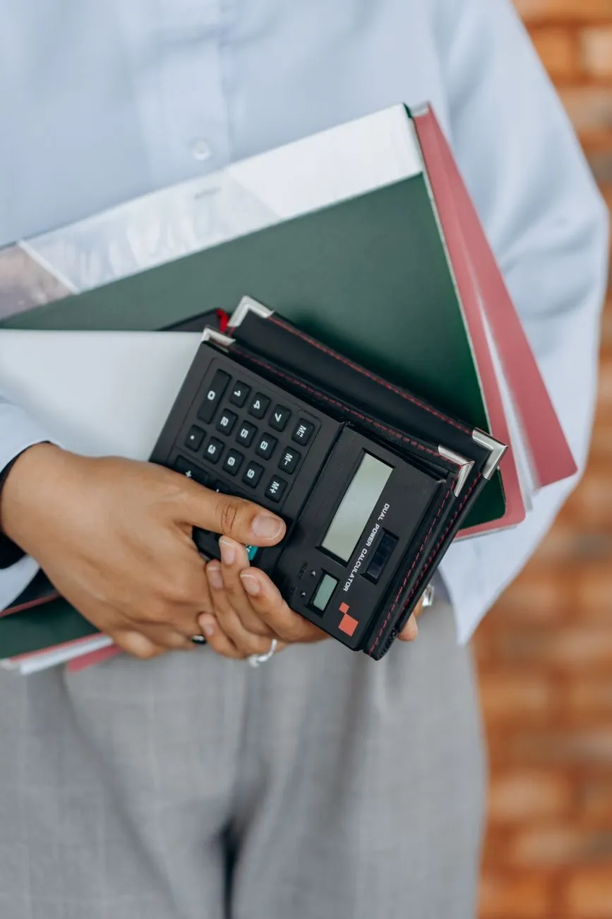 A member of the team carrying folders and a calculator, photographed from the shoulders down