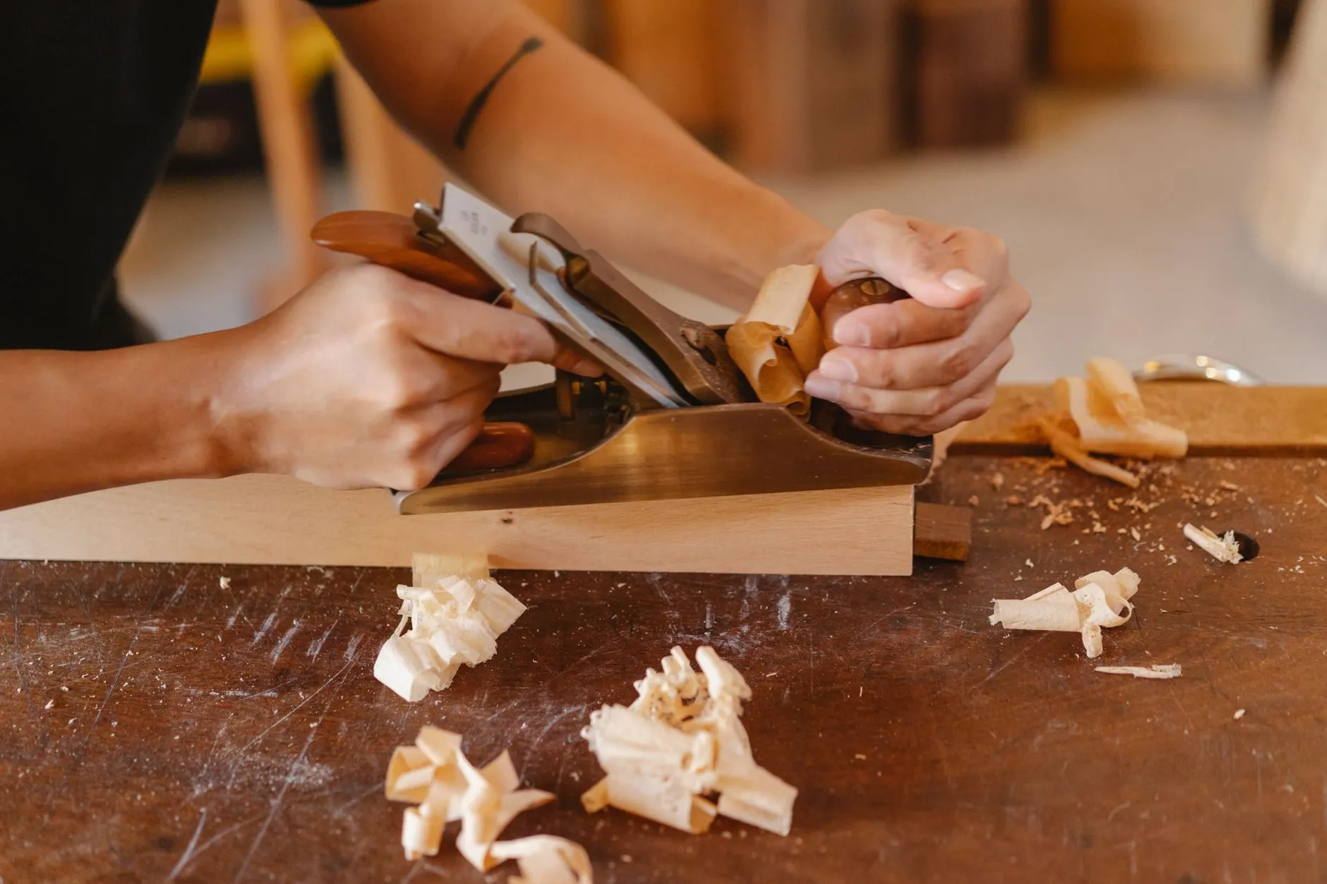 A joiner planing a length of timber at a workbench, shavings curling off the blade