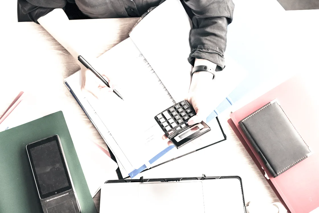 A desk with a bound analysis ledger, a pen and a laptop under even light
